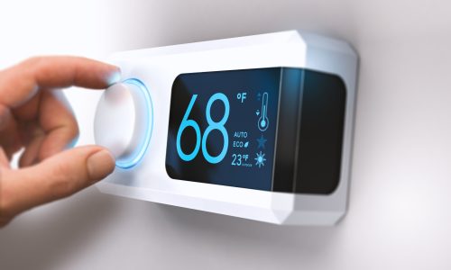 Hand turning a home thermostat knob to set temperature on energy saving mode. fahrenheit units. Composite image between a photography and a 3D background.